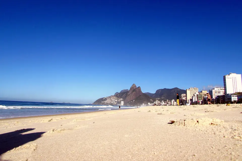 La playa de Ipanema en Río de Janeiro, con los cerros Dois Irmãos al fondo y arena vacía bajo un cielo celeste sin nubes