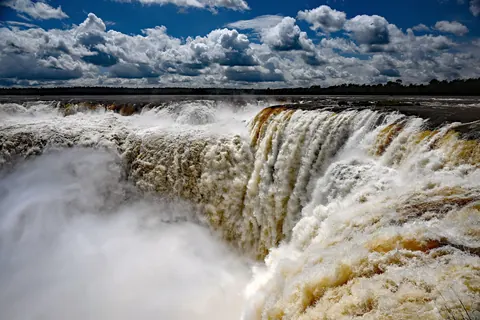 La Garganta del Diablo en las Cataratas del Iguazú, con el agua cayendo entre la espuma blanca y un cielo de nubes dramáticas