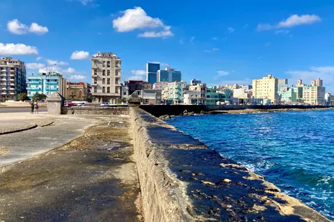 El Malecón de La Habana: el muro de piedra junto al mar azul y, al fondo, los edificios del Vedado bajo un cielo con nubes