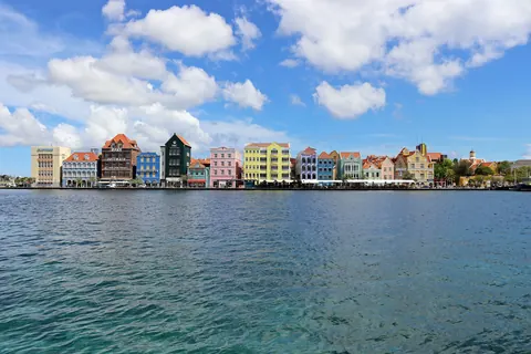 Las fachadas de colores del Handelskade, en Willemstad, Curazao, vistas desde el agua de la bahía bajo un cielo azul con nubes