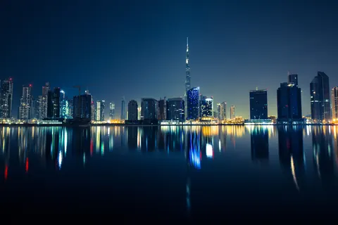 Skyline nocturno de Dubái con el Burj Khalifa iluminado en el centro y los rascacielos reflejados en el agua en calma