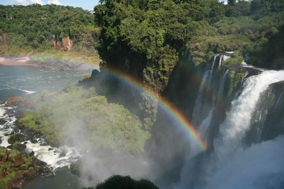 Un arco iris se forma sobre las Cataratas del Iguazú, con varios saltos de agua cayendo entre la selva verde, del lado argentino