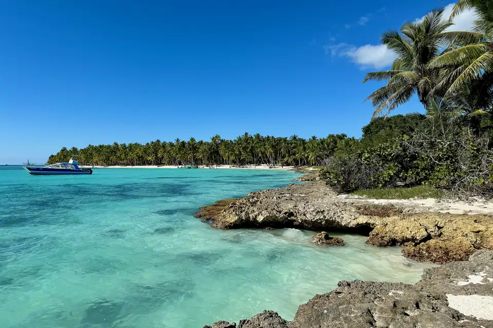 Punta rocosa cubierta de palmeras en Isla Saona, República Dominicana, con un bote anclado en el agua turquesa transparente