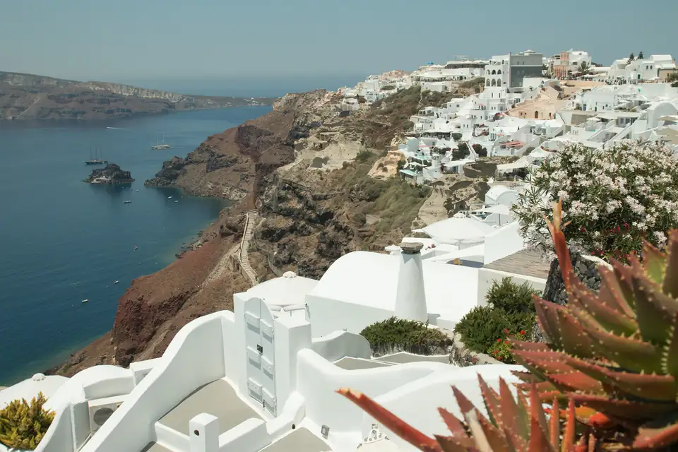 El pueblo blanco de Oia se derrama por el acantilado de la caldera de Santorini, con veleros anclados en el mar azul profundo