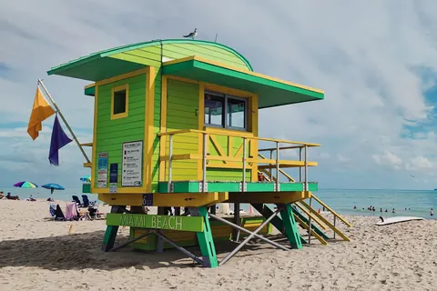 Caseta de guardavidas verde y amarilla sobre la arena de South Beach, Miami, con el mar turquesa y el cielo despejado de fondo